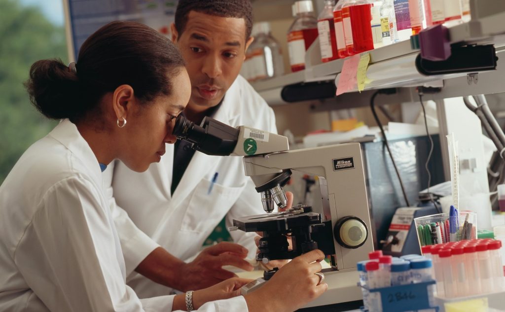 female research student using a microscope beside a male